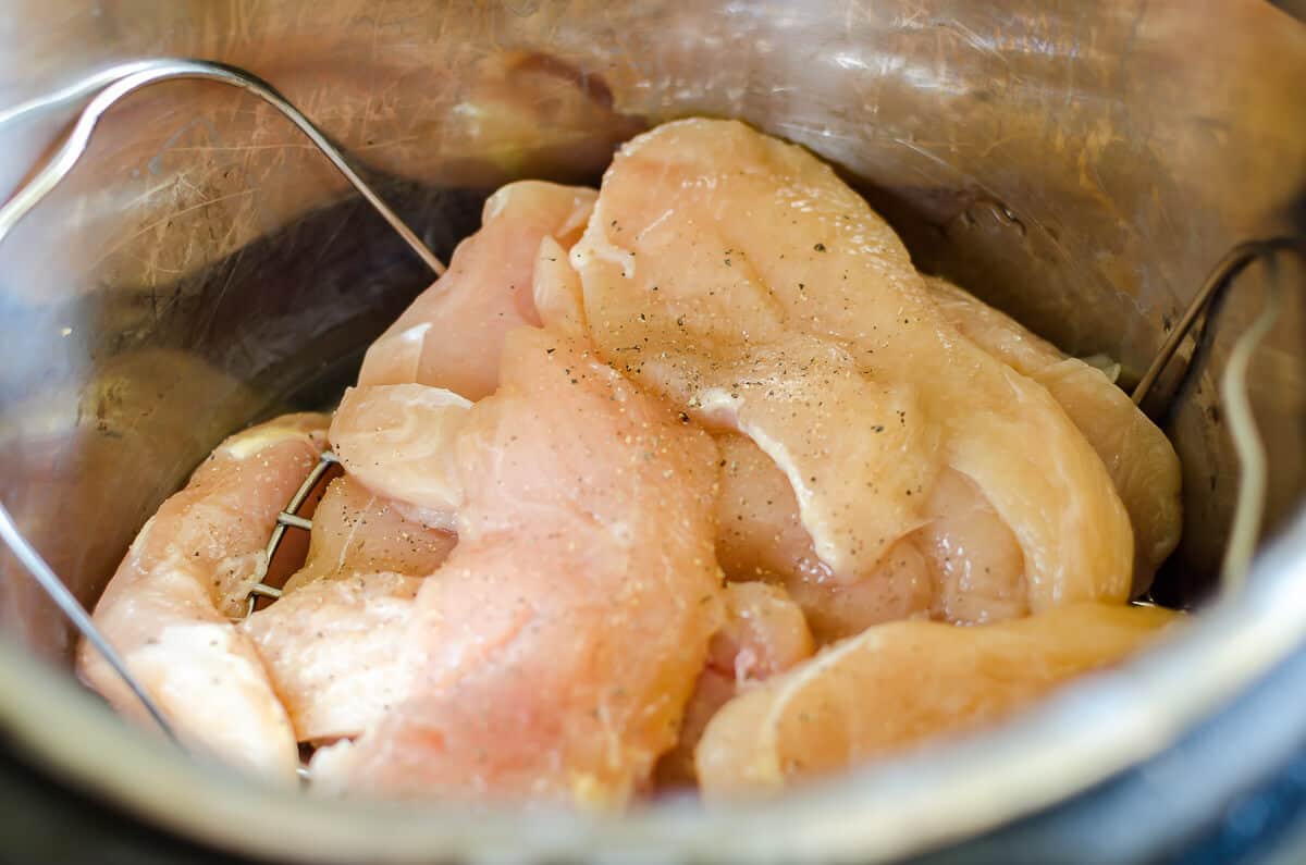 raw chicken breasts inside the Instant Pot seasoned with salt and pepper