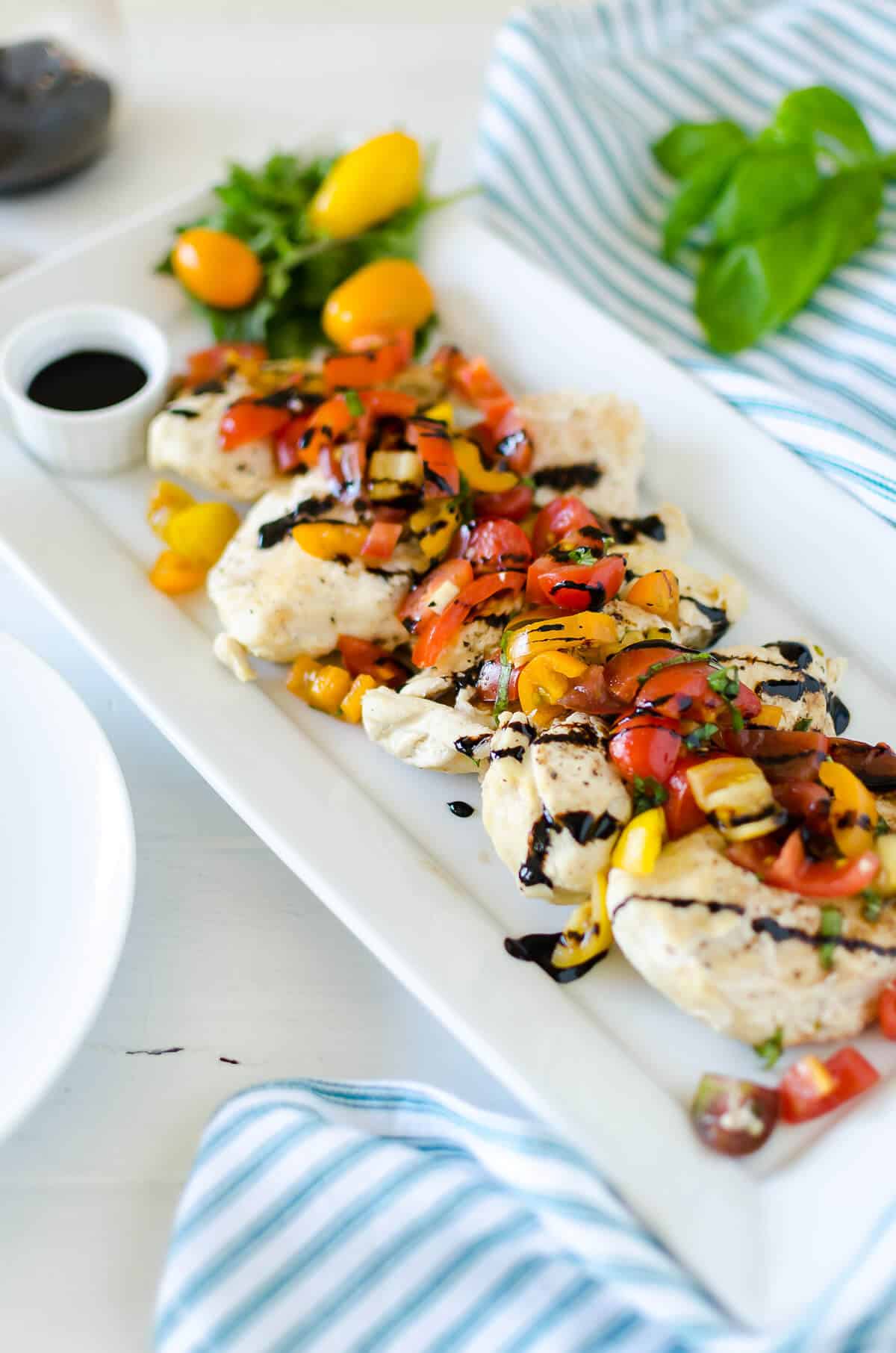 rectangle white platter with tender chicken breasts topped with marinated tomatoes, basil, and garlic and topped with balsamic vinegar drizzle. Instant Pot Bruschetta Chicken