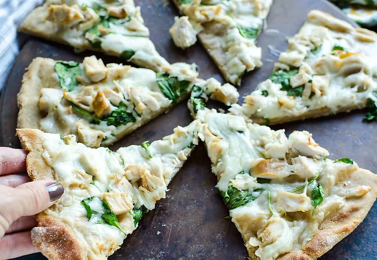 several pieces of hot homemade white pizza with a hand reaching in grabbing a piece.