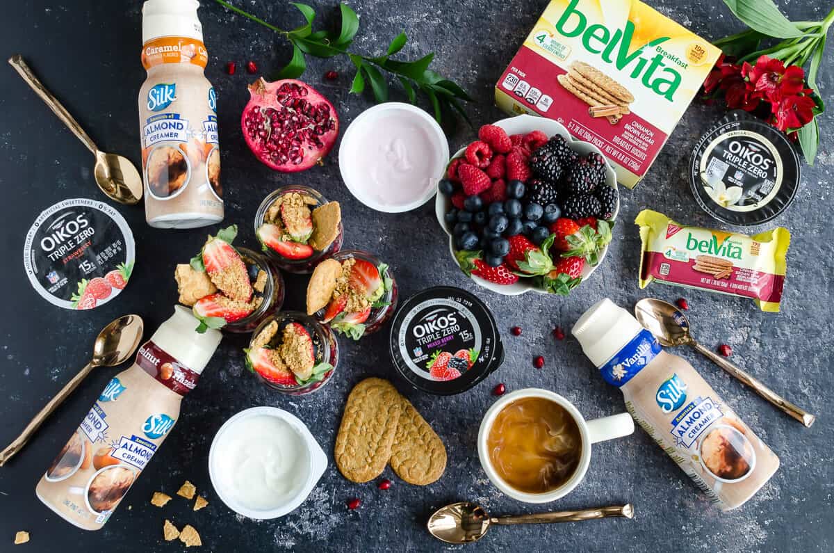 breakfast spread overhead view of silk creamers, breakfast chia pudding, fresh berries, belVita breakfast biscuits, Oikos triple zero yogurt, coffee cup with cream, gold spoons