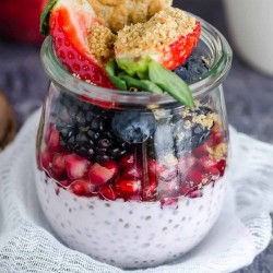 glass jar layered with chia seed pudding, pomegranate arils, blackberries, blueberries, strawberries, and crumbled belVita breakfast biscuit