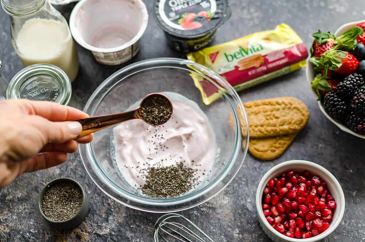 bowl of mixed berry yogurt with teaspoon of chia seeds being poured into the yogurt
