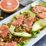 chopped brussels sprouts salad on a rectangle white platter with caramelized onions, grapefruit segments, avocado slices, and pistachios