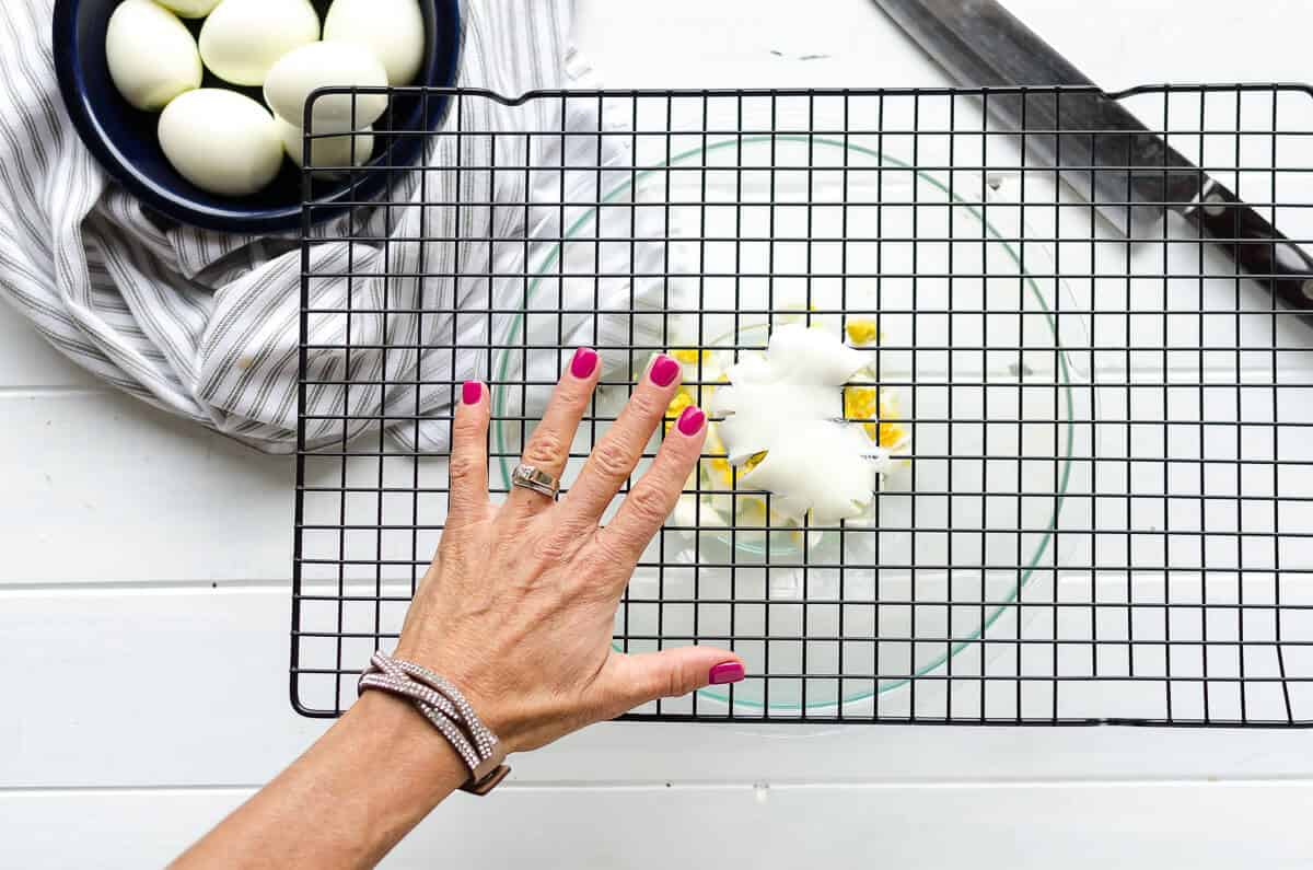 bowl with cookie rack on top to show chopping eggs hack, egg is being pushed through the grid.