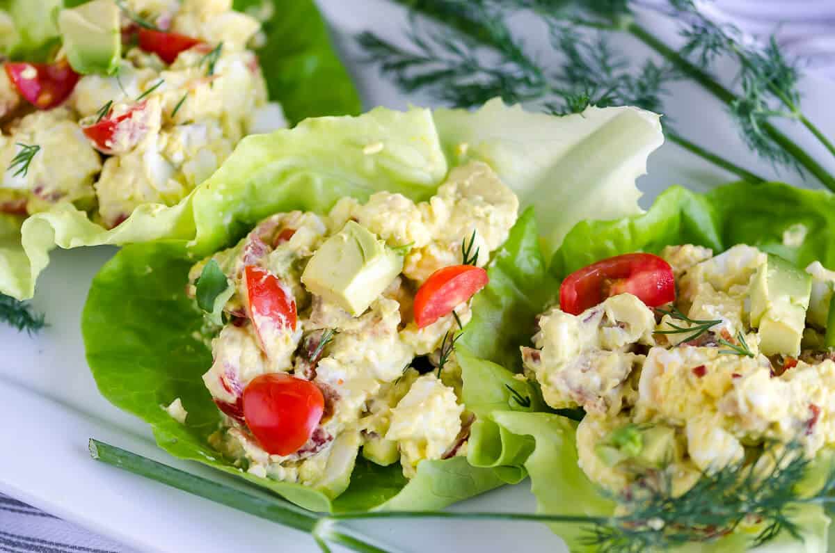 egg salad with chopped tomatoes, avocados, bacon, and blue cheese in a lettuce cup garnished with fresh dill