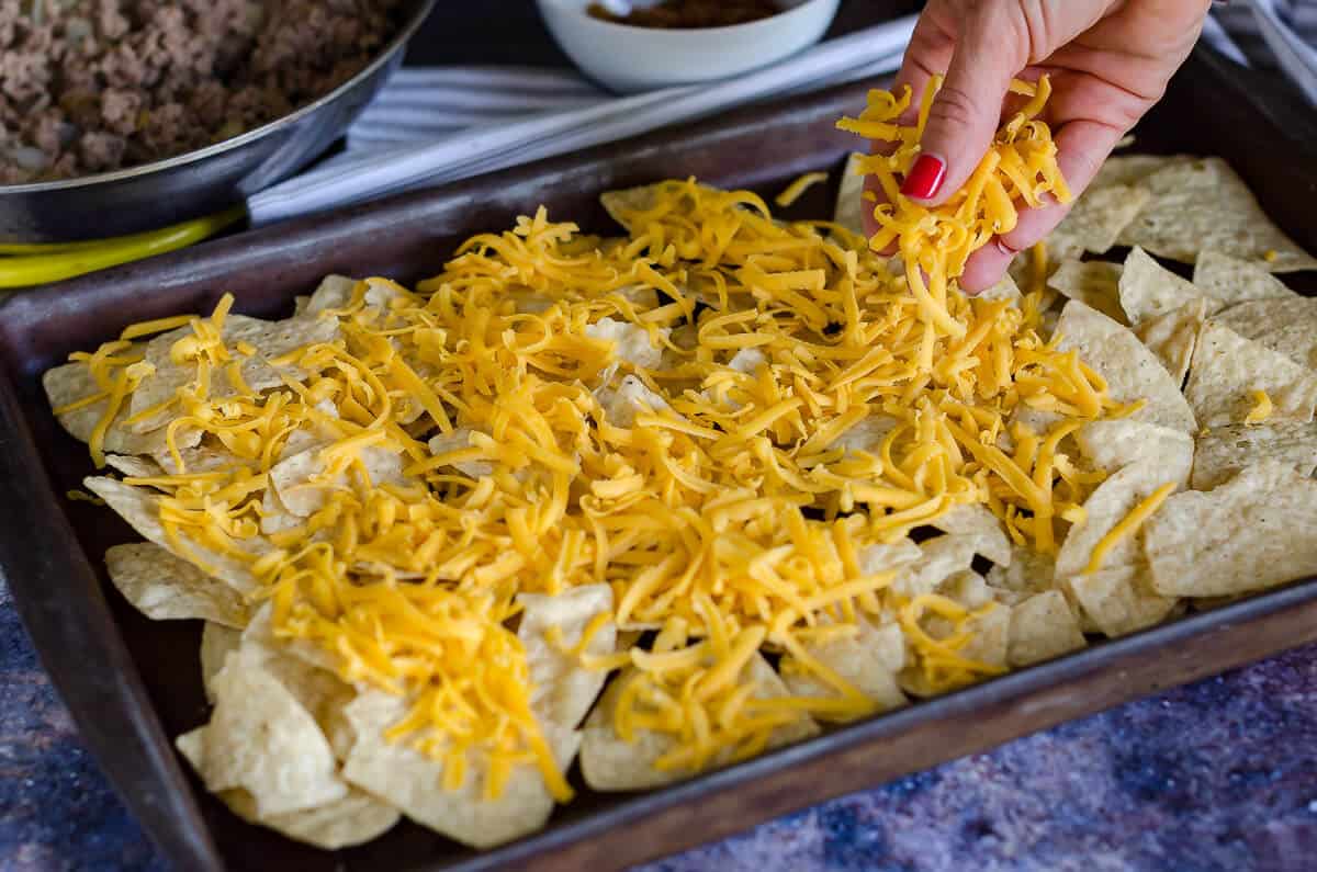hand placing shredded cheese on a pan of tortilla chips not baked yet.