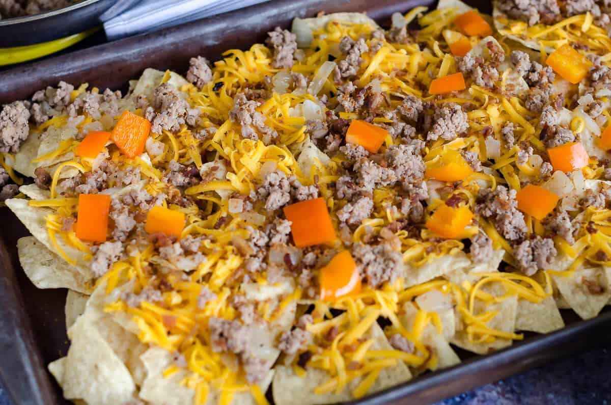 pan of tortilla chips with shredded cheese, ground turkey, onions, crumbled bacon and orange bell peppers not baked yet.