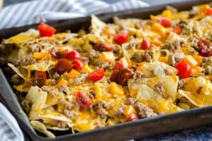 sheet pan of cheeseburger nachos with peppers and tomatoes