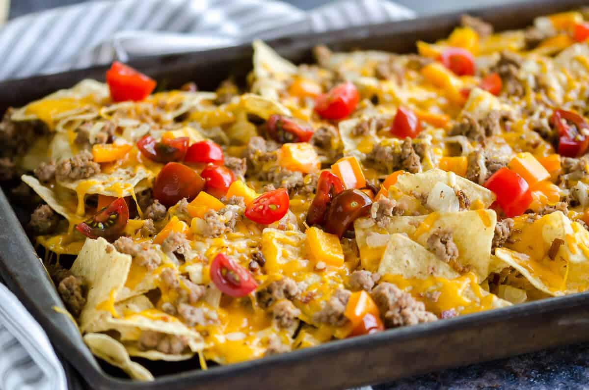 sheet pan of cheeseburger nachos with peppers and tomatoes