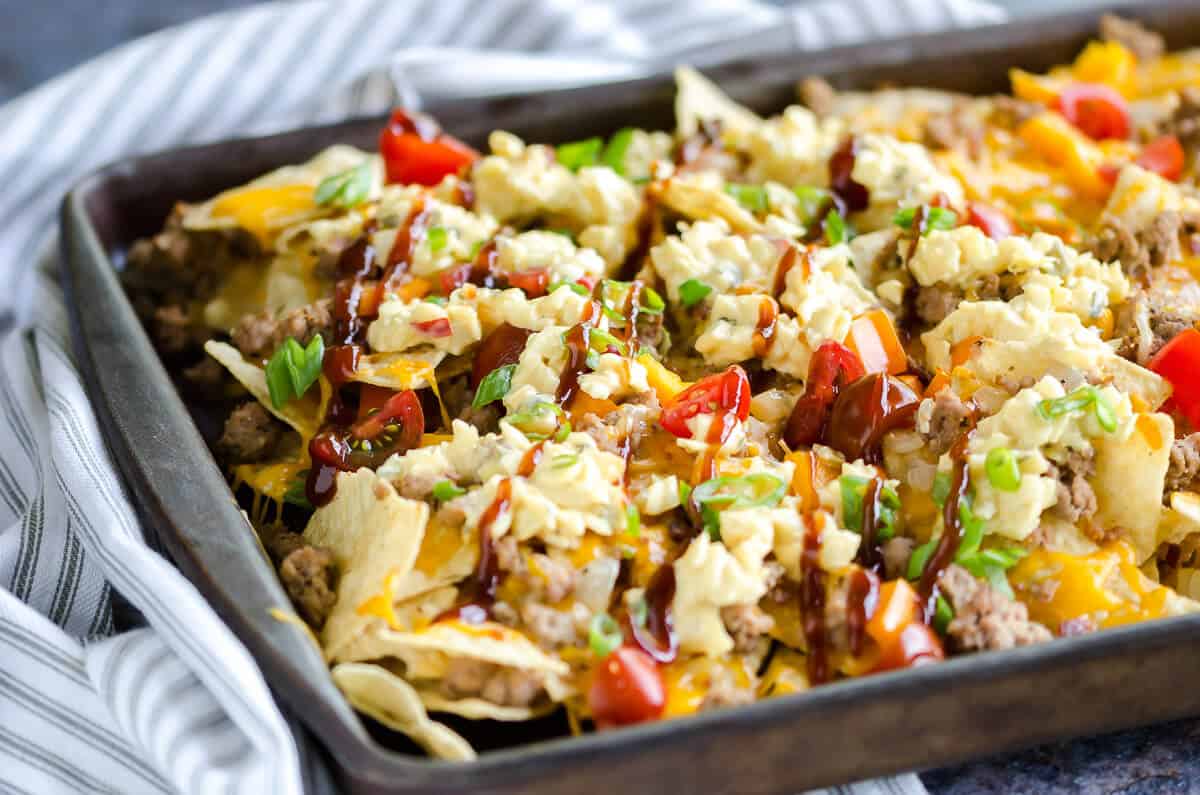 sheet pan of bbq bacon cheeseburger nachos made with ground turkey, topped with cole slaw and drizzled with bbq sauce