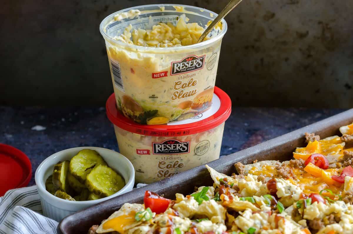 2 containers of resers stadium cole slaw stacked. The one on top opened with a spoon in it. sitting next to a pan of cheeseburger nachos with ground turkey