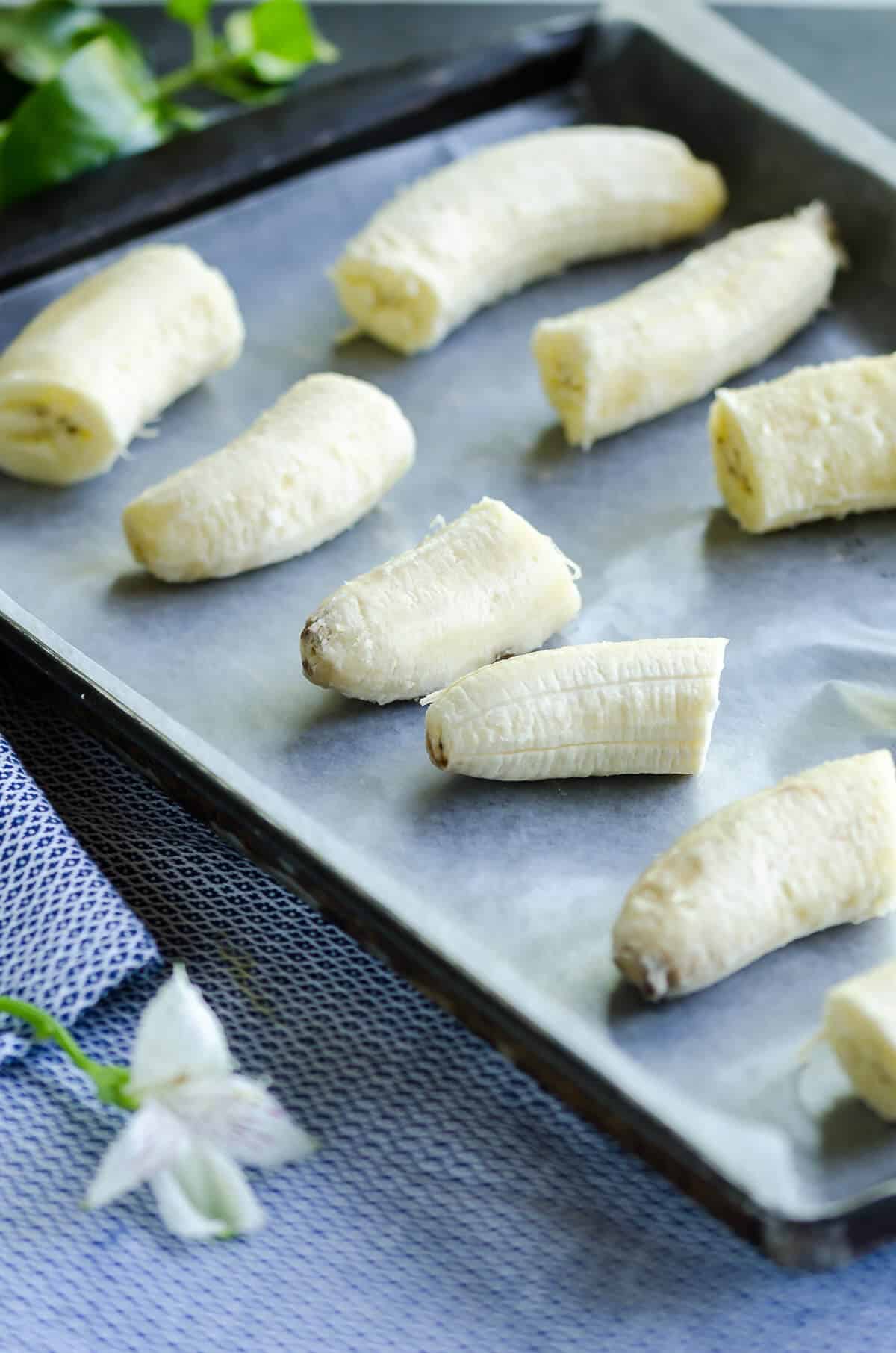 peeled bananas cut into thirds on a wax paper lined baking sheet ready to freeze.