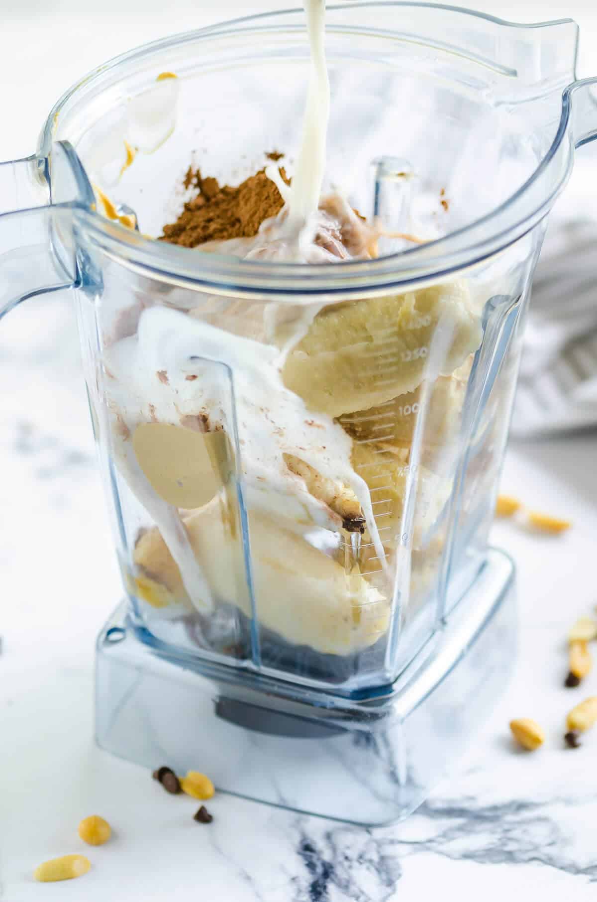 blender filled with frozen bananas, coco powder, almond milk and peanut butter