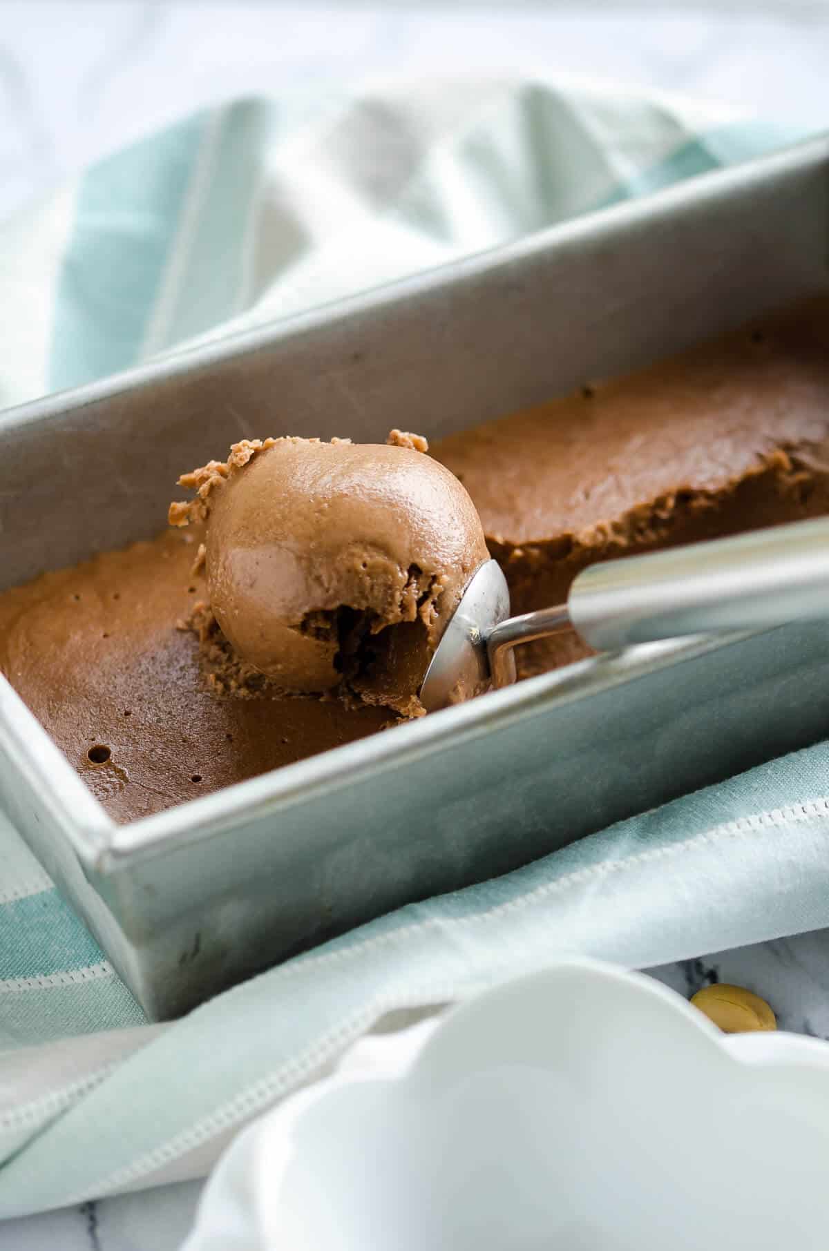 ice cream scoop scooping out 4 ingredient chocolate peanut butter banana ice cream out of a loaf pan.