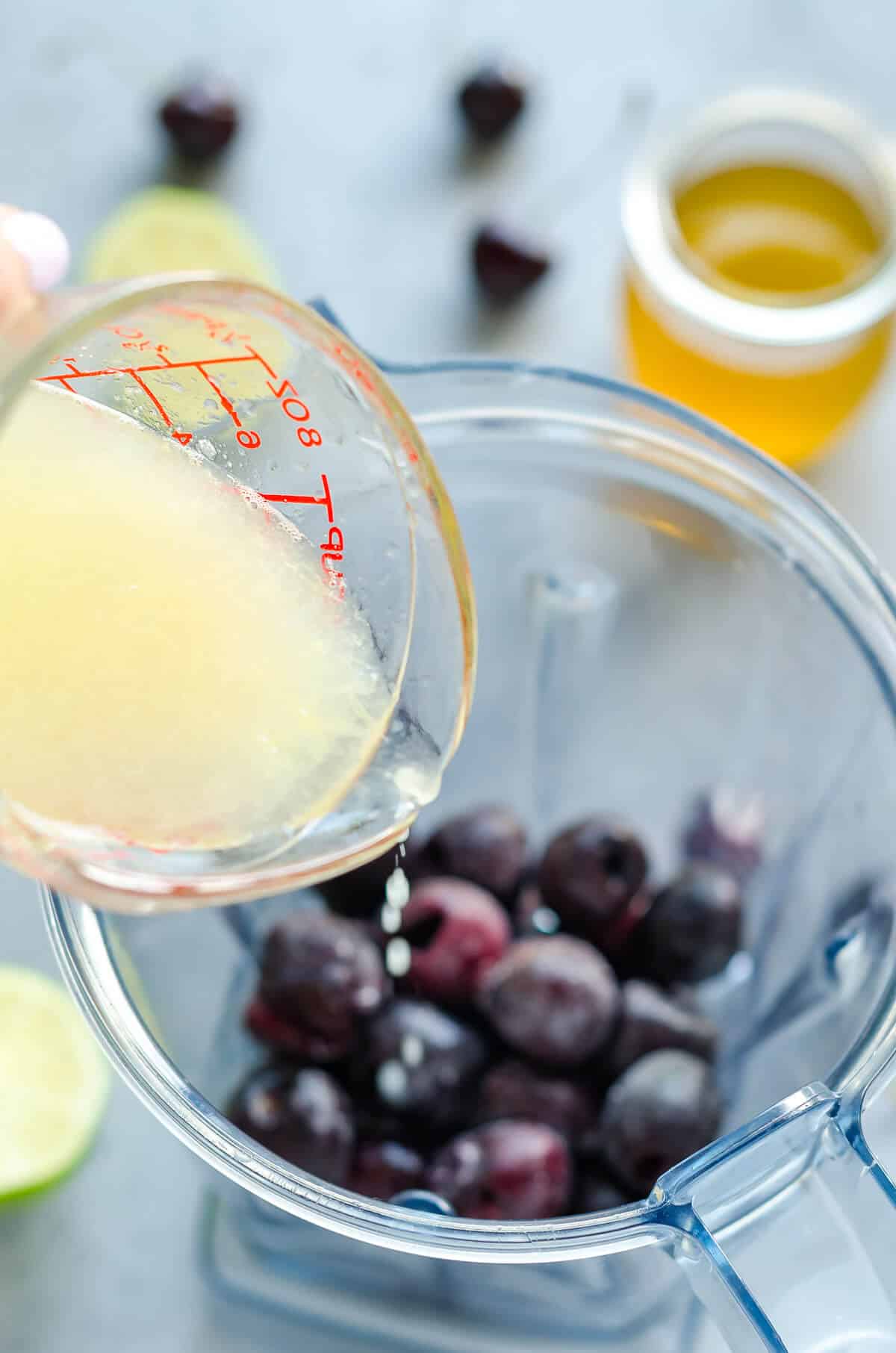 frozen sweet cherries in a blender with lime juice being poured in.
