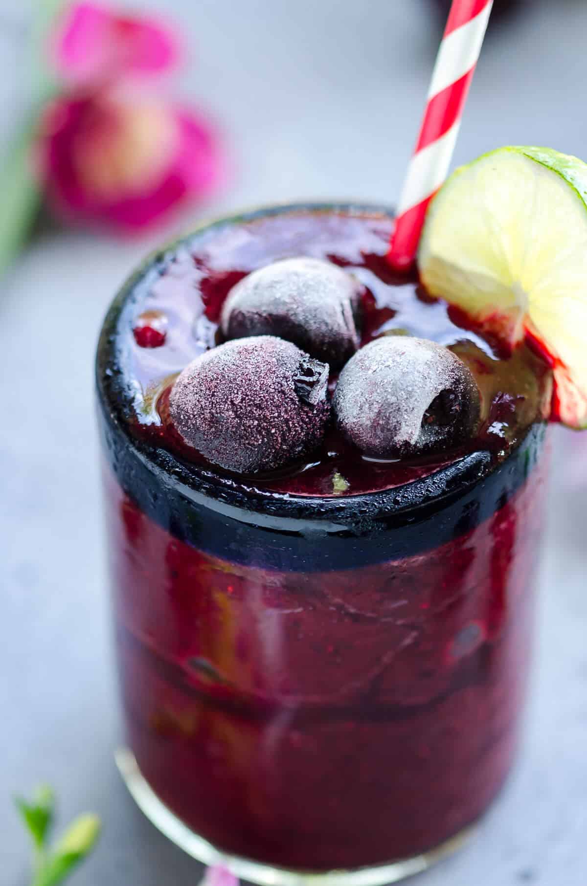 deep red frozen cherry cooler filled to the brim of a clear glass topped with frosty frozen sweet cherries and garnished with slice of lime on the side of the glass