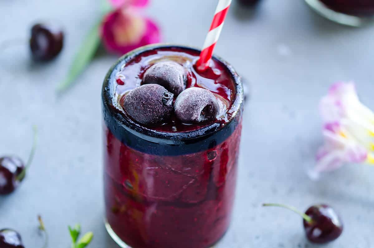 Frozen cherry cooler beverage in a clear glass topped with frosty sweet cherries. red and white striped straw