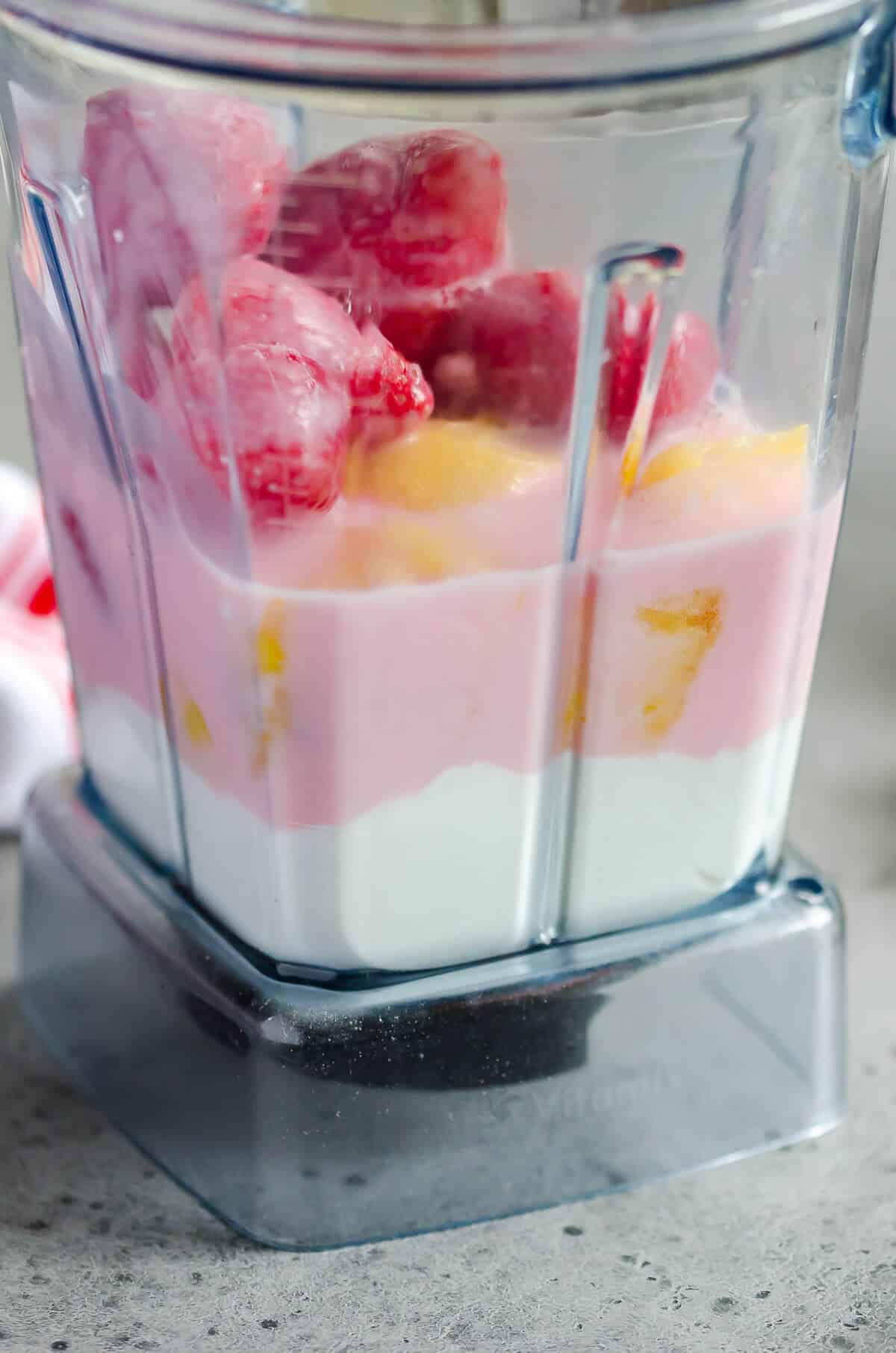 Blender layered with yogurt, strawberry milk, frozen pineapples, and frozen strawberries