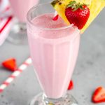 milkshake glass filled with strawberry pineapple smoothie, garnished with a slice of pineapple and a strawberry