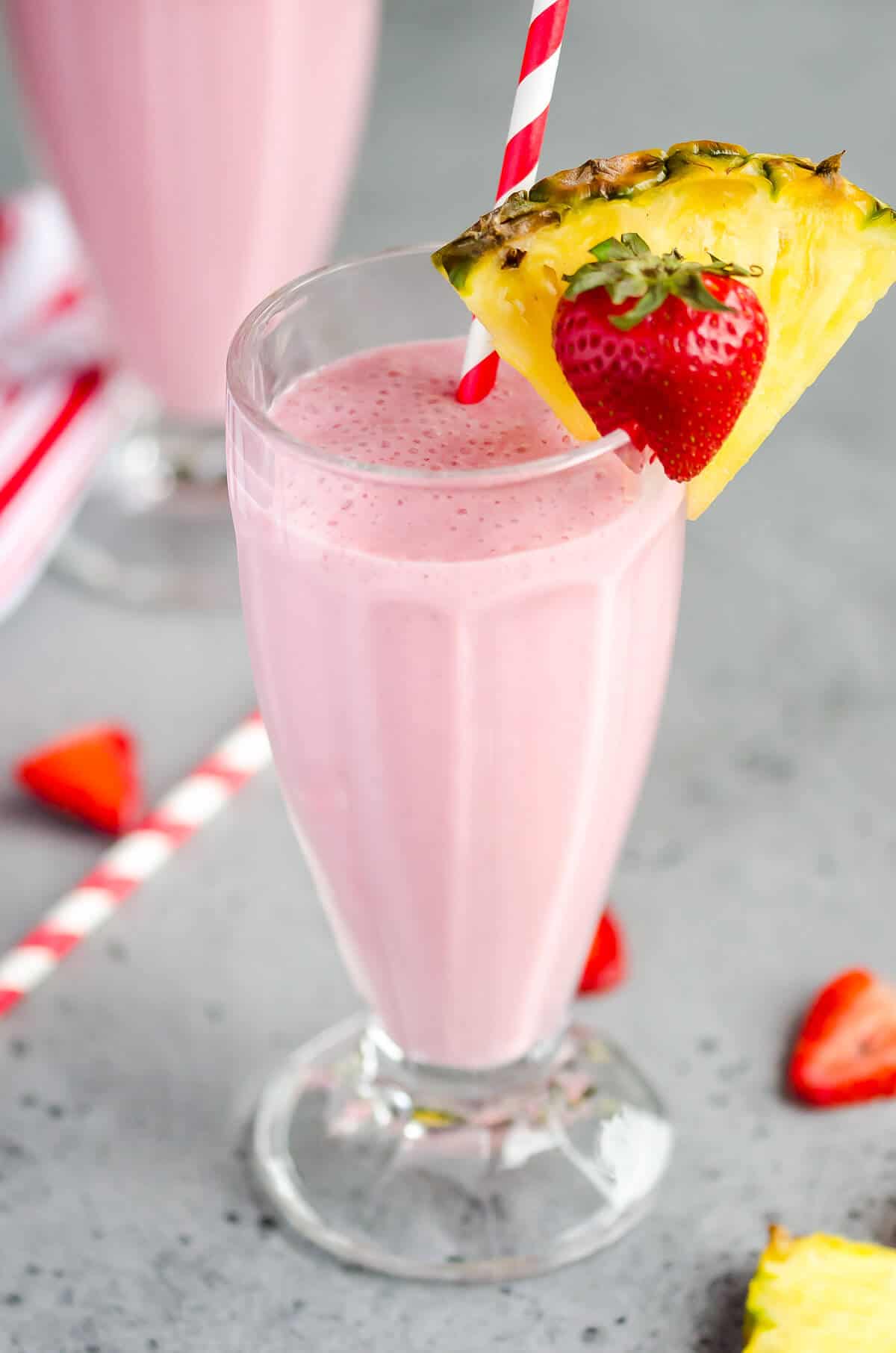milkshake glass filled with strawberry pineapple smoothie, garnished with a slice of pineapple and a strawberry