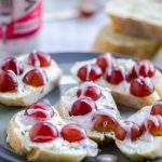 plate full of goat cheese crostini with grapes drizzled with strawberry poppyseed dressing. Baguettes and dressing in the background