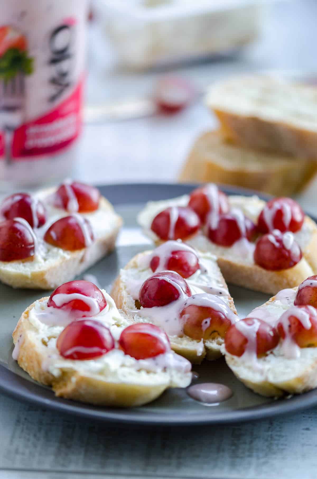 plate full of goat cheese crostini with grapes drizzled with strawberry poppyseed dressing. Baguettes and dressing in the background