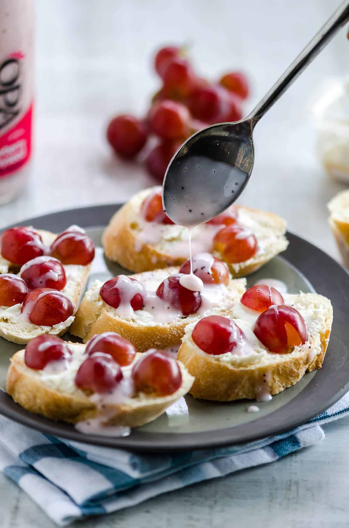spoon drizzling strawberry poppyseed dressing over the top of a plate full of goat cheese crostini with grapes.