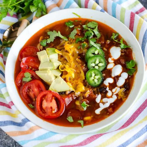 bowl of turkey taco soup garnished with sliced cherry tomatoes, avocados, cheese, jalapeños, and yogurt