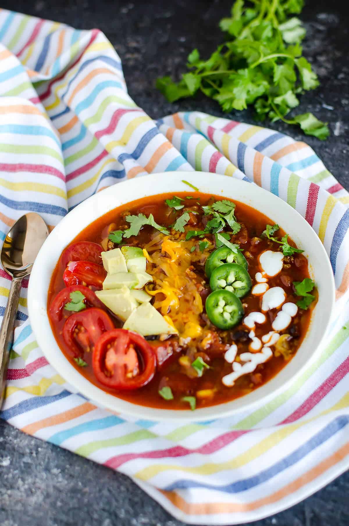 Bowl of taco soup garnished with sliced cherry tomatoes, avocados, cheese, jalapeños, and yogurt