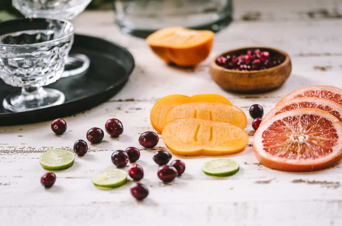 fruta fresca para mocktail de sangría roja, incluyendo lima en rodajas, arándanos frescos, caqui en rodajas y pomelo en rodajas