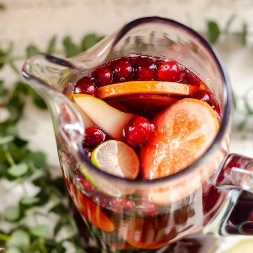 overhead view of a pitcher filled with red Sangria Mocktail, grapefruit, limes, pears and cranberries