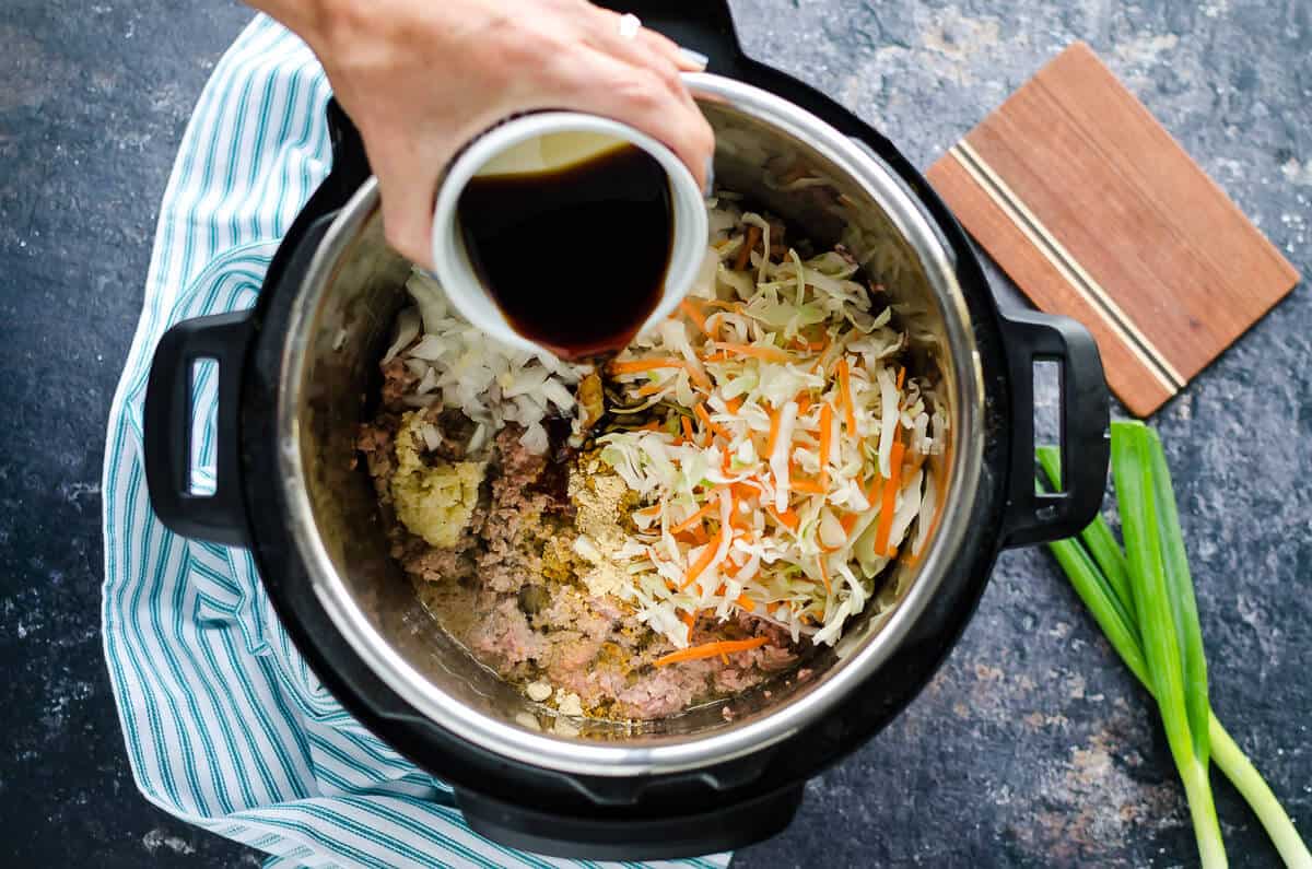 hand pouring soy sauce into an instant pot filled with ground turkey, shredded cabbage and shredded carrots
