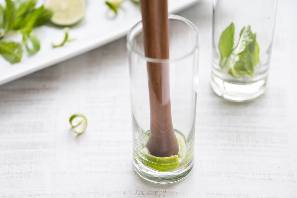 fresh lime and mint being muddled in a glass