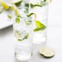 two mojito mocktails in clear glasses with fresh mint and lime