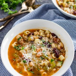 two white bowls of pasta fagioli soup garnished with parmesan cheese and parsley