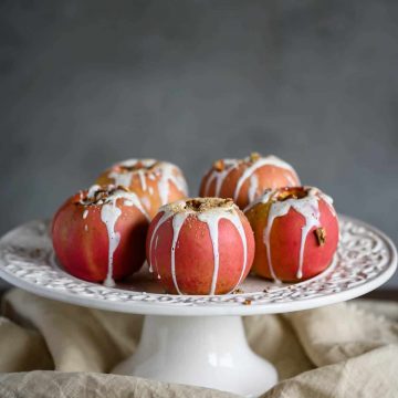 healthy baked apples drizzled with sweet yogurt sauce, pecans and cinnamon on a cake pedestal
