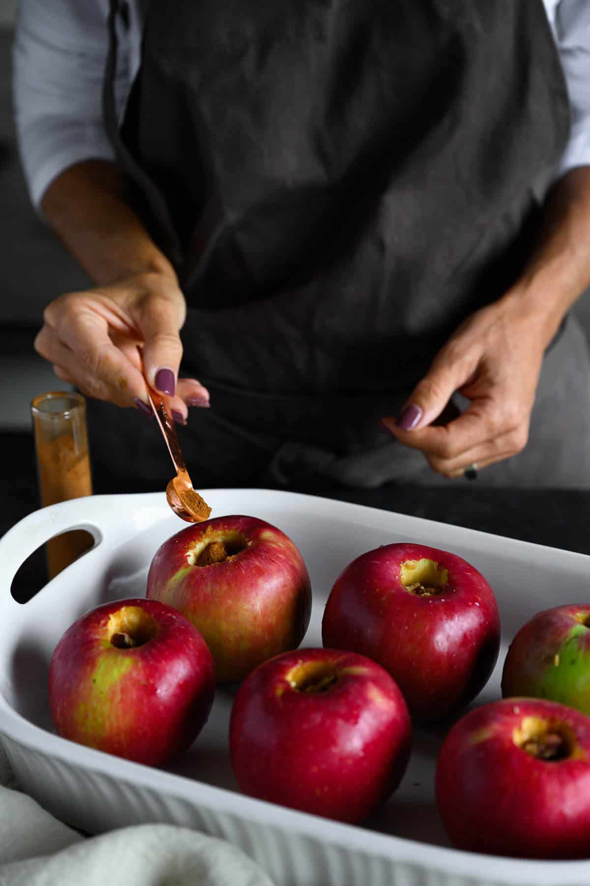 woman sprinkling cinnamon over whole cored apples for baking.