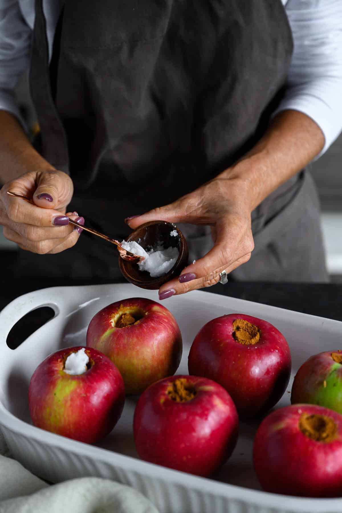 woman putting coconut oil on top of stuffed apples before going in the oven.
