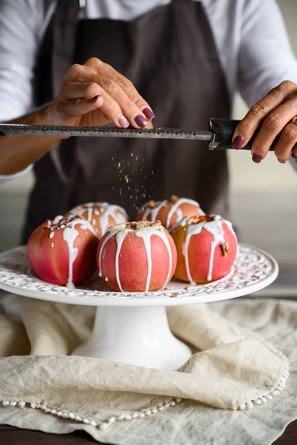 woman using a microplane to grate fresh nutmeg over baked apples