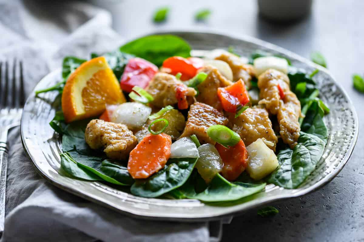 crockpot orange chicken served over a bed of spinach.