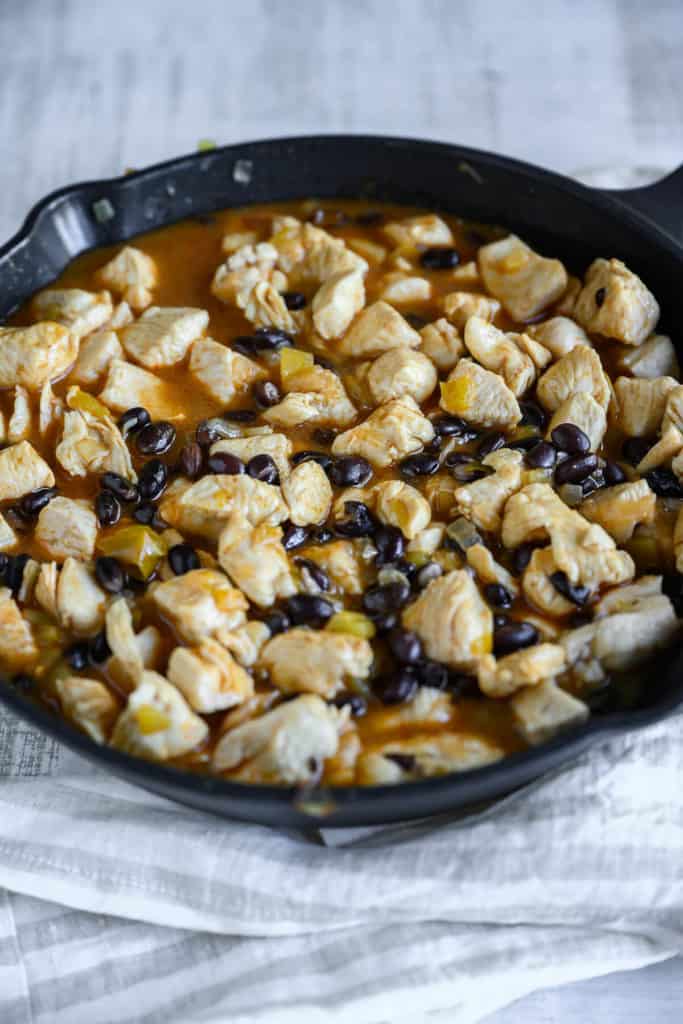 skillet with chicken, black beans, chili peppers and enchilada sauce