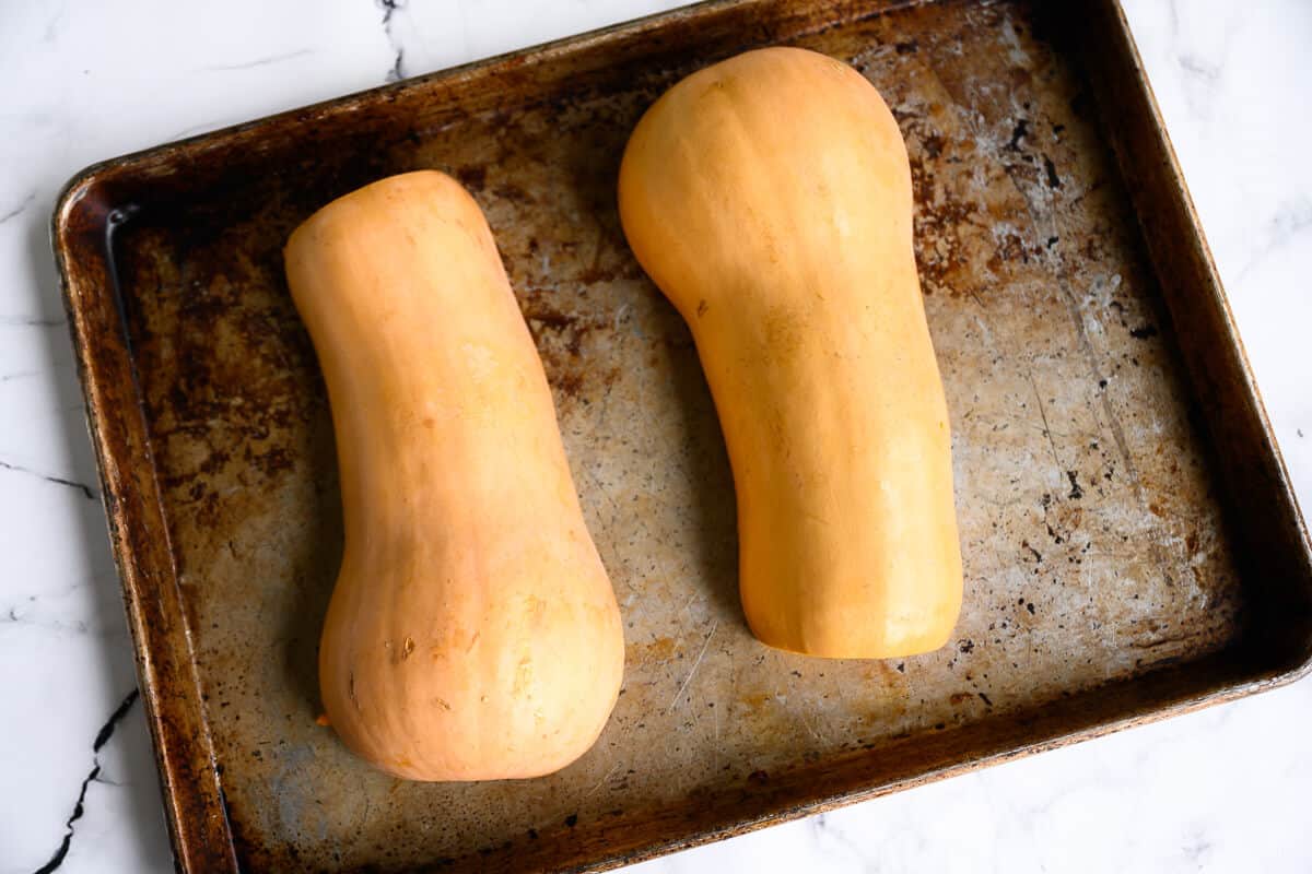 butternut squash cut in half lengthwise on a rimmed baking sheet skin side down