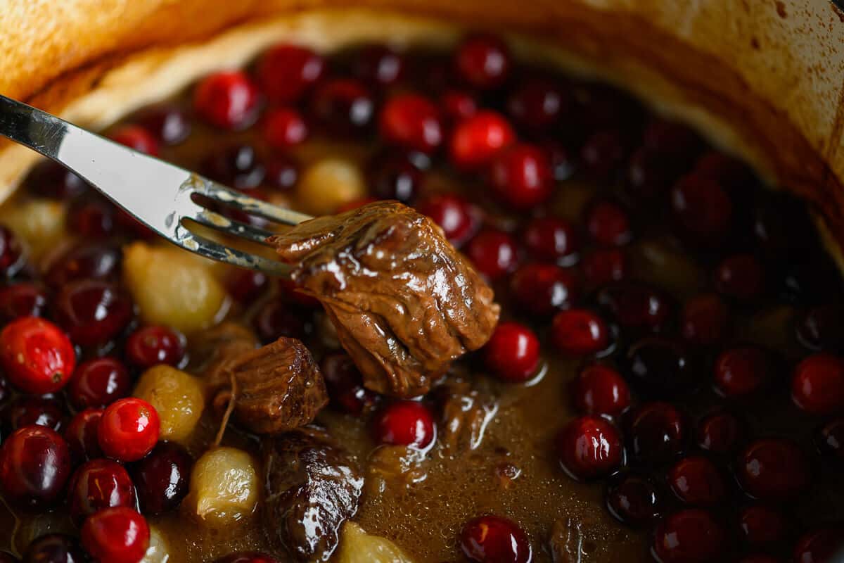 tender chunk of braised beef on a fork over a dutch oven