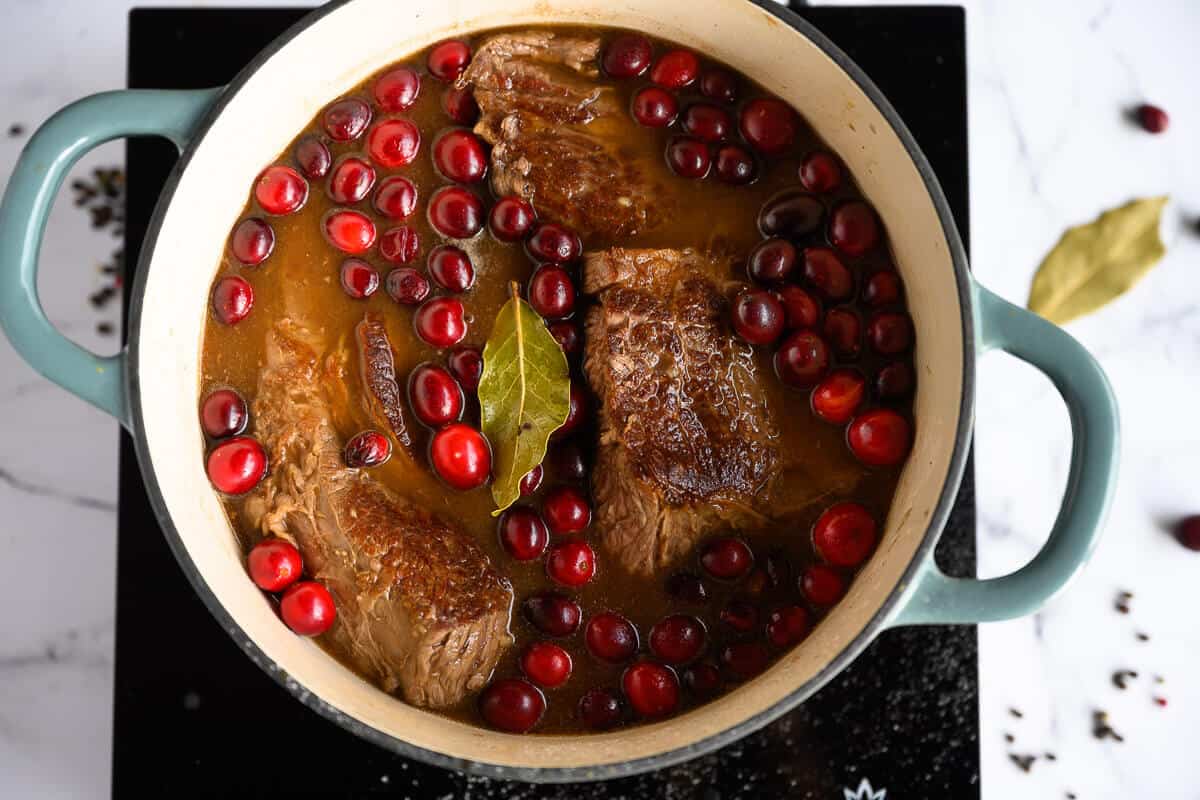 dutch oven full of braised beef roast, cranberries, bay leaf