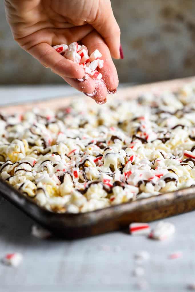 crushed peppermint sticks being sprinkled over chocolate drizzled popcorn