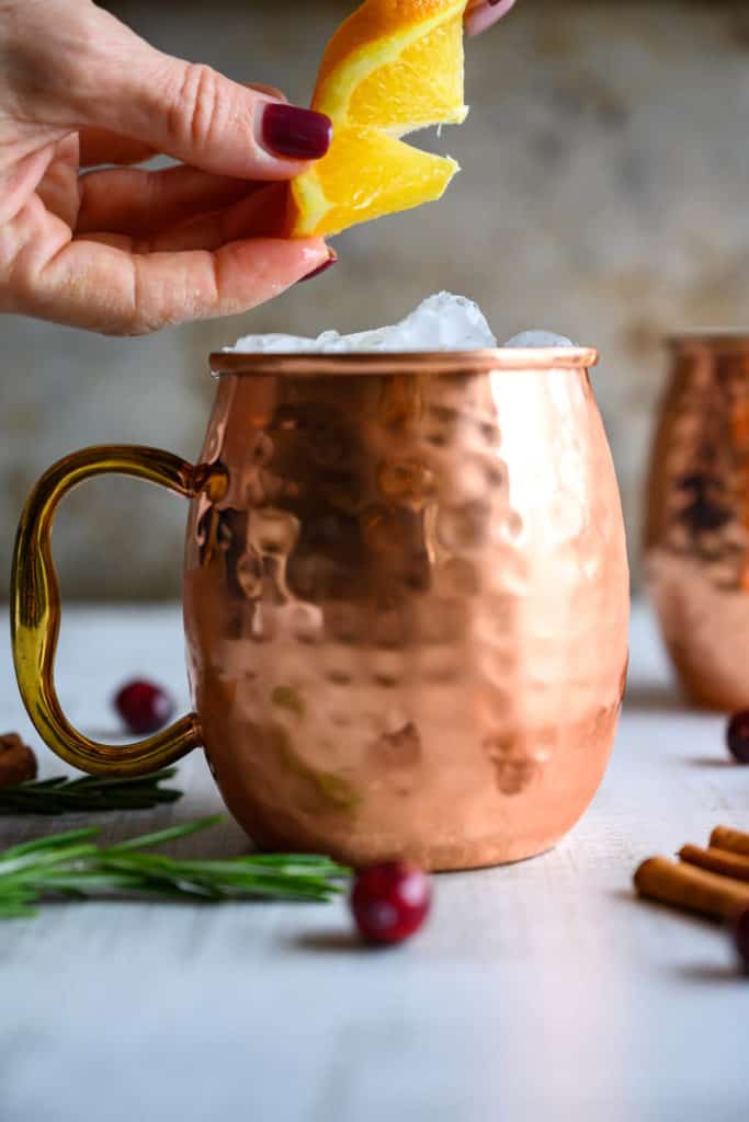 fresh orange wedge being squeezed and twisted over crushed ice in a hammered copper mug