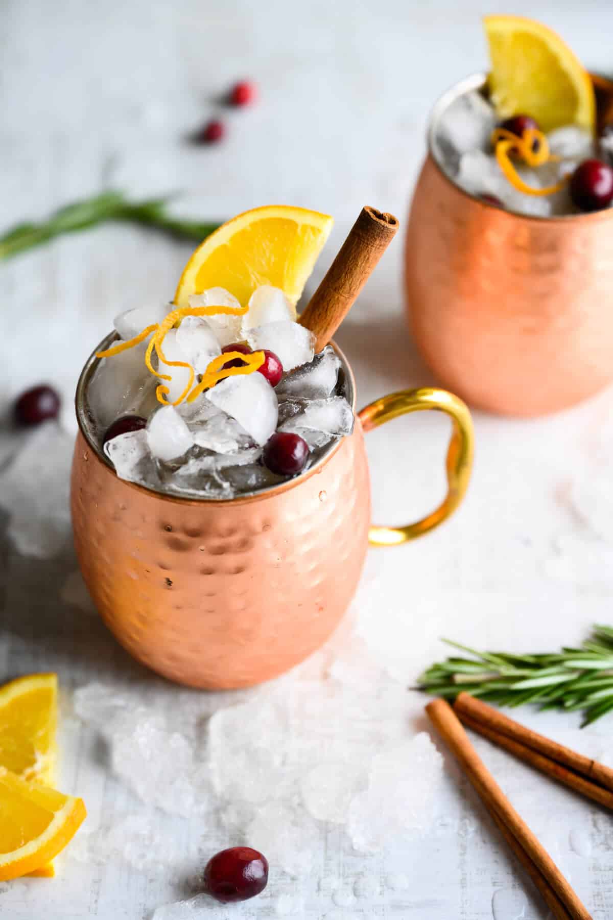 non-alcoholic cranberry moscow mule in a copper mug, garnished with orange peel, orange wedge, and cinnamon stick