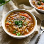 two steaming bowls of lentil soup garnished with pepper and parsley