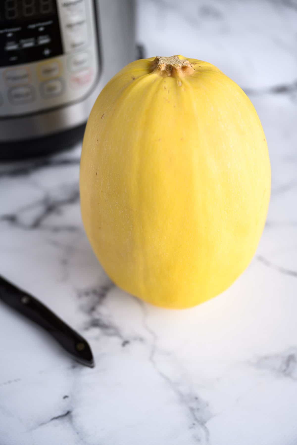 whole spaghetti squash standing upright in front of instant pot
