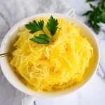 Cooked Spaghetti Squash "noodles' in a white bowl, garnished with a sprig of parsley